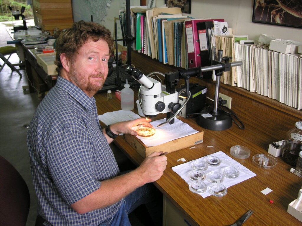 Photo of Robert Anderson sitting at a desk next to a microscope.
