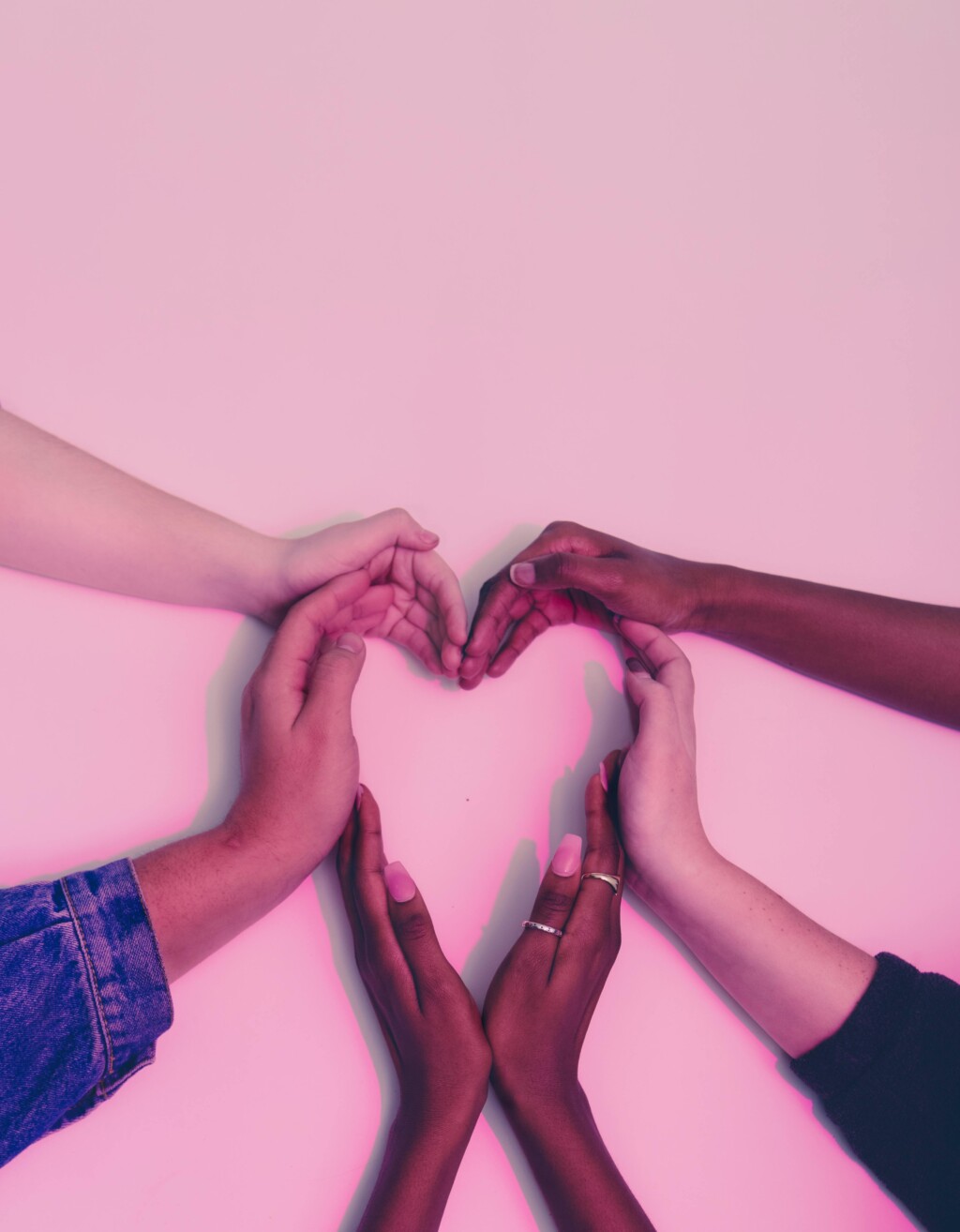 Photo of four hands forming the shape of a heart with a pink background