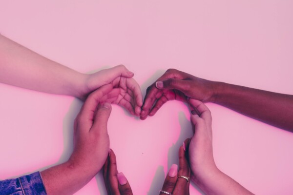 Photo of four hands forming the shape of a heart with a pink background