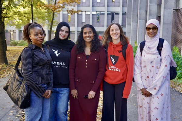Photo of five Carleton students standing outside of Herzberg Laboratories in the fall.