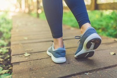 Image of a close up of female legs with running shoes on wooden footpath in woods. Nature and sport healthy lifestyle concept.